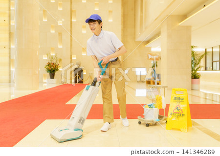 一位年輕的日本男清潔工正在用吸塵器打掃辦公大樓。照片由東京電子電波學園提供。 一位年輕的日本男清潔工正在用吸塵器打掃辦公大樓。照片由東京電子電波學園提供。 141346289