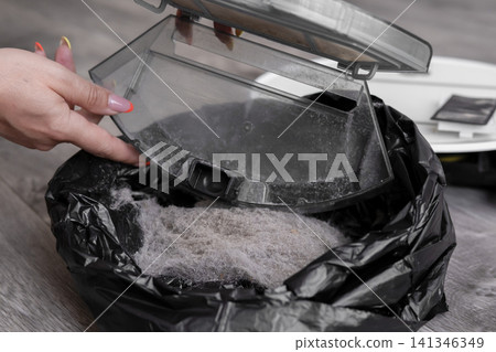Close up of woman hand emptying full robot vacuum dustbin into black garbage bag Close up of woman hand emptying full robot vacuum dustbin into black garbage bag 141346349