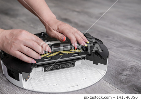 Close up of woman hands opening main brush cover of robot vacuum cleaner Close up of woman hands opening main brush cover of robot vacuum cleaner 141346350