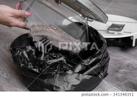 Close up of woman hand emptying full robot vacuum dustbin into black garbage bag Close up of woman hand emptying full robot vacuum dustbin into black garbage bag 141346351