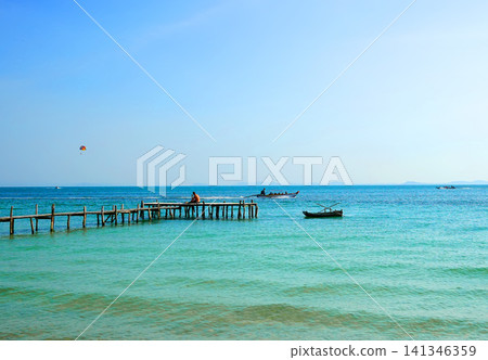 Tropical landscape with turquoise ocean water, wooden pier, and fishing boats Tropical landscape with turquoise ocean water, wooden pier, and fishing boats 141346359