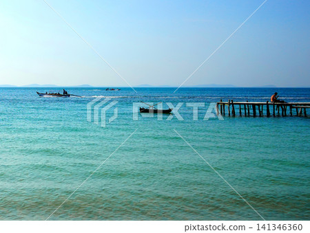 Tropical landscape with turquoise ocean water, wooden pier, and fishing boats Tropical landscape with turquoise ocean water, wooden pier, and fishing boats 141346360