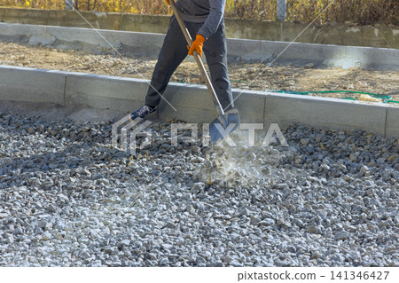 Worker is using shovel to move gravel at construction site at renovation road Worker is using shovel to move gravel at construction site at renovation road 141346427