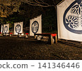 A night view of Koishikawa Korakuen Garden, January 2024, featuring a banner bearing the Tokugawa family crest of three hollyhock leaves and benches covered with red cloth. 141346446