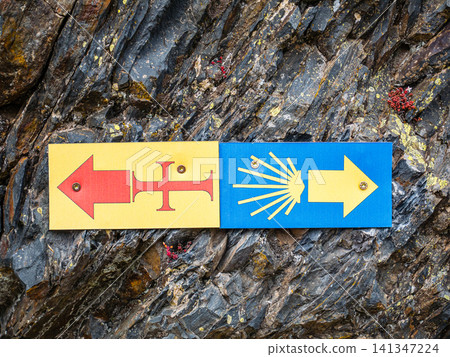 Camino de Santiago waymark sign with arrows on a natural rock face Camino de Santiago waymark sign with arrows on a natural rock face 141347224