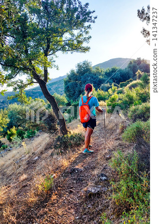 Female hiker walking on a sun-drenched mountain trail 141347237