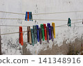 Colorful plastic clothespins clipped onto multiple outdoor clotheslines against a weathered white wall. Vibrant laundry pegs. Everyday household scene with rustic textures, natural lighting 141348916