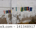 Colorful plastic clothespins clipped onto multiple outdoor clotheslines against a weathered white wall. Vibrant laundry pegs. Everyday household scene with rustic textures, natural lighting 141348917