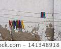 Colorful plastic clothespins clipped onto multiple outdoor clotheslines against a weathered white wall. Vibrant laundry pegs. Everyday household scene with rustic textures, natural lighting 141348918