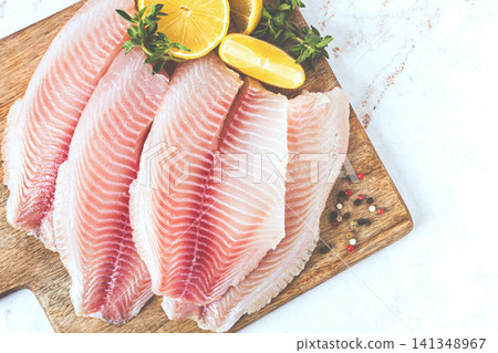 Fresh Tilapia fillet, on a wooden chopping board, with lemon and herbs, ready to cook in the kitchen, no people 141348967