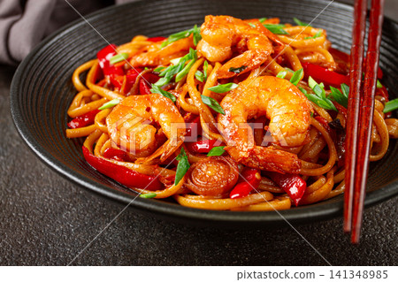 udon stir-fry shrimp noodles with red bell pepper and green onion, served in a black bowl, with chopsticks, dark background, udon stir-fry shrimp noodles with red bell pepper and green onion, served in a black bowl, with chopsticks, dark background, 141348985