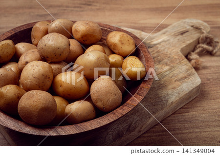 Freshly harvested small potatoes in a wooden bowl on a rustic cutting board in a kitchen setting Freshly harvested small potatoes in a wooden bowl on a rustic cutting board in a kitchen setting 141349004