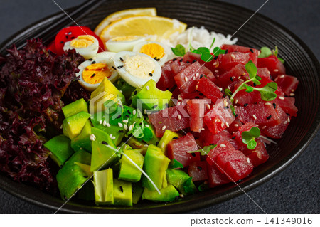 Fresh poke bowl with tuna, avocado, and vegetables served on a black plate Fresh poke bowl with tuna, avocado, and vegetables served on a black plate 141349016