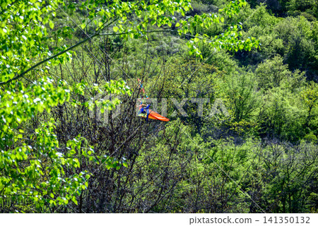 Orange glider above green forest hillside Orange glider above green forest hillside 141350132