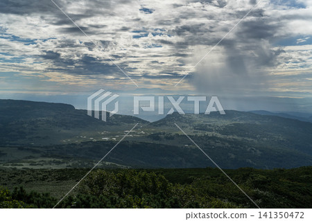 Rain clouds and a plain bathed in light, viewed from the mountaintop. Rain clouds and a plain bathed in light, viewed from the mountaintop. 141350472