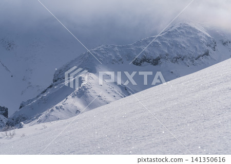 A dramatic landscape of clouds swirling over snow-covered volcanic ridges. 141350616