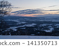 A snow-covered plain and a winding river stretch out beneath the sunset sky. 141350713