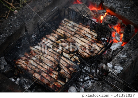 Unrecognizable man cooking seafood on a barbecue grill in the backyard. Unrecognizable man cooking seafood on a barbecue grill in the backyard. 141351027