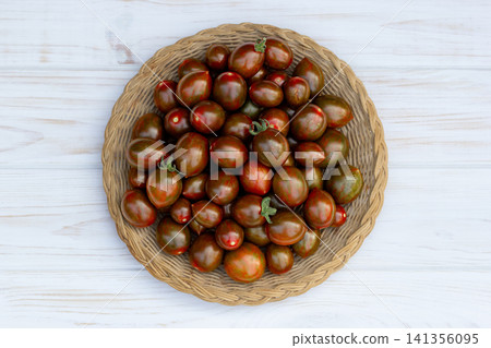 Dark cherry tomatoes in the woven plate on the white table. Dark cherry tomatoes in the woven plate on the white table. 141356095