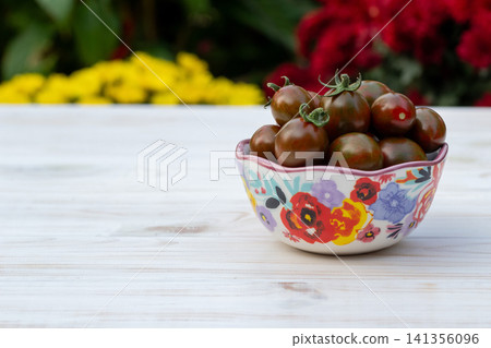 Bowl with black cherry tomatoes in the summer blooming garden. Bowl with black cherry tomatoes in the summer blooming garden. 141356096