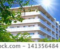 A white, newly built apartment building seen through the dazzling sun and fresh greenery. 141356484