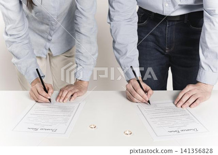 Divorce Agreement Signing with Wedding Rings on Table Divorce Agreement Signing with Wedding Rings on Table 141356828