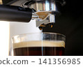 Close-up of an espresso machine brewing freshly extracted black coffee into a clear glass cup, highlighting coffee preparation 141356985