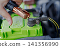 Hand holding jumper cable clamp near car battery 141356990