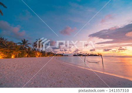 Sunset beach with palm trees and swing hammock silhouette on tropical island. Warm resort lights glowing under colorful evening sky, calm sea at dusk. Romantic paradise twilight scene for travel Sunset beach with palm trees and swing hammock silhouette on tropical island. Warm resort lights glowing under colorful evening sky, calm sea at dusk. Romantic paradise twilight scene for travel 141357310