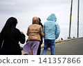 People walking uphill on a mountain road wearing winter jackets and casual clothing 141357866