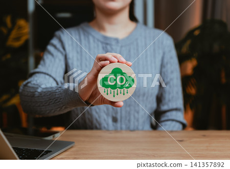 Carbon footprint reduction and sustainability concept. Person holding wooden icon featuring CO2 cloud, symbolizing eco-friendly actions, climate change awareness and environmental responsibility. Carbon footprint reduction and sustainability concept. Person holding wooden icon featuring CO2 cloud, symbolizing eco-friendly actions, climate change awareness and environmental responsibility. 141357892