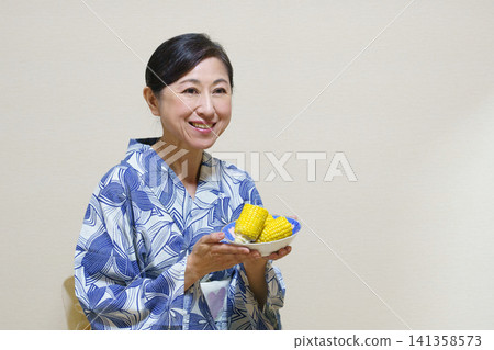 A senior woman wearing a yukata offers boiled corn. A senior woman wearing a yukata offers boiled corn. 141358573