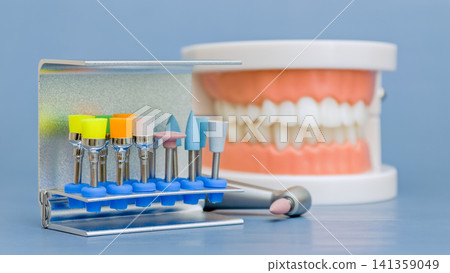 Colorful dental polishing brushes and silicone cups in a metal stand with a blurred tooth model on a blue background. Colorful dental polishing brushes and silicone cups in a metal stand with a blurred tooth model on a blue background. 141359049