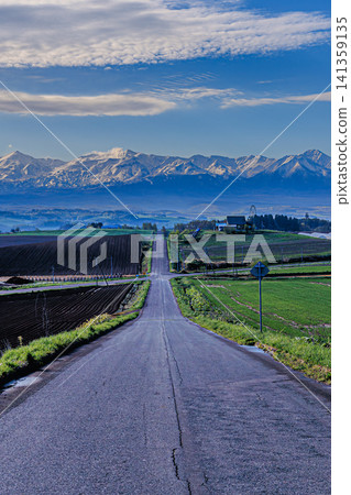 在蔚藍的天空下,一條通往北海道美瑛町上富良野的道路,以及十勝山脈的壯麗景色盡收眼底。 在蔚藍的天空下,一條通往北海道美瑛町上富良野的道路,以及十勝山脈的壯麗景色盡收眼底。 141359135