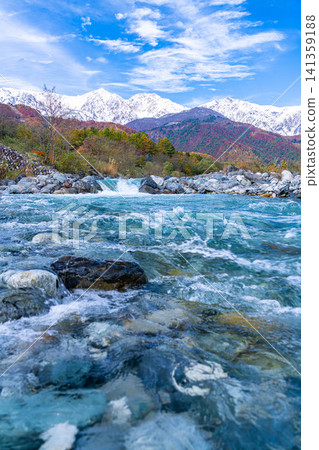 Autumn foliage on the mountains and the snow-capped Ushirotateyama mountain range as seen from near Hakuba Ohashi Bridge in Hakuba Village [Nagano Prefecture] 141359188