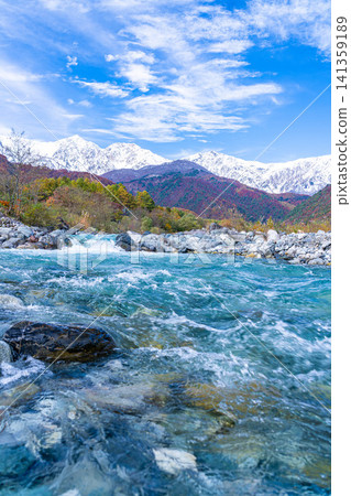 Autumn foliage on the mountains and the snow-capped Ushirotateyama mountain range as seen from near Hakuba Ohashi Bridge in Hakuba Village [Nagano Prefecture] 141359189