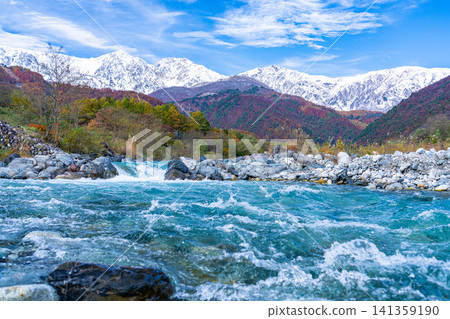 Autumn foliage on the mountains and the snow-capped Ushirotateyama mountain range as seen from near Hakuba Ohashi Bridge in Hakuba Village [Nagano Prefecture] 141359190