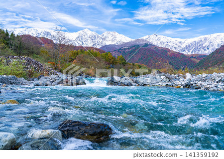 Autumn foliage on the mountains and the snow-capped Ushirotateyama mountain range as seen from near Hakuba Ohashi Bridge in Hakuba Village [Nagano Prefecture] 141359192