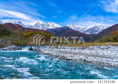 Autumn foliage on the mountains and the snow-capped Ushirotateyama mountain range as seen from near Hakuba Ohashi Bridge in Hakuba Village [Nagano Prefecture] 141359196