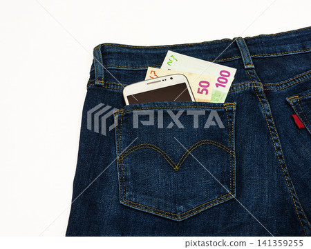 In the pants pocket of a blue denim is a smartphone and banknotes In the pants pocket of a blue denim is a smartphone and banknotes 141359255