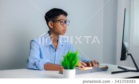 Asian man with glasses looking at computer screen and typing on keyboard at home office. Concentrated smart student studying online or software developer working on technology project. Asian man with glasses looking at computer screen and typing on keyboard at home office. Concentrated smart student studying online or software developer working on technology project. 141359383