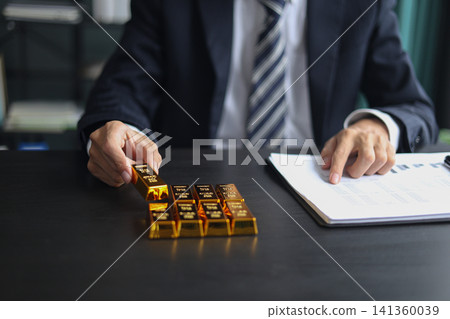 Gold investment Concept. Businessman working on financial planning and gold investment analysis with bullion on desk. Gold investment Concept. Businessman working on financial planning and gold investment analysis with bullion on desk. 141360039