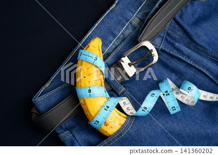 Banana with measuring tape on jean trousers, penis health. Banana with measuring tape on jean trousers, penis health. 141360202