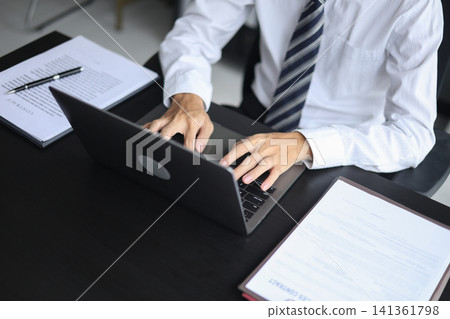 Professional lawyer reviewing a legal business contract while working on laptop in modern office. Professional lawyer reviewing a legal business contract while working on laptop in modern office. 141361798