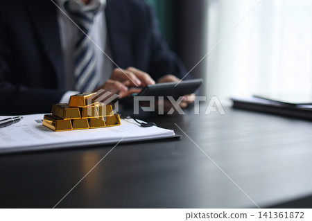 Gold investment Concept. Businessman working on financial planning and gold investment analysis with bullion and calculator. Gold investment Concept. Businessman working on financial planning and gold investment analysis with bullion and calculator. 141361872