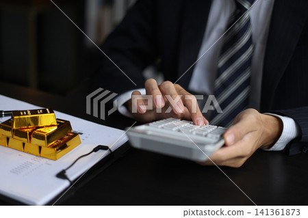 Gold volatility. Businessman calculating profit from fine gold bar investments. Gold volatility. Businessman calculating profit from fine gold bar investments. 141361873
