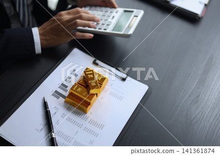 Gold investment Concept. Businessman working on financial planning and gold investment analysis with bullion and calculator. Gold investment Concept. Businessman working on financial planning and gold investment analysis with bullion and calculator. 141361874