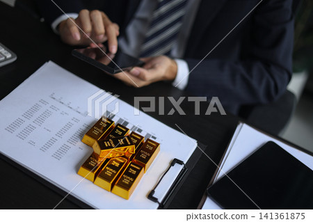 Gold volatility. Businessman calculating profit from fine gold bar investments. Gold volatility. Businessman calculating profit from fine gold bar investments. 141361875