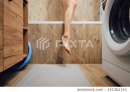 Female foot hanging over edge of bathtub in modern bathroom Female foot hanging over edge of bathtub in modern bathroom 141362141