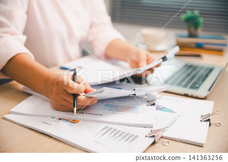 Close-up hands reviewing printed business charts with pen on office desk, showing financial report, accounting paperwork, market analysis, budget planning, data research, and corporate review. Close-up hands reviewing printed business charts with pen on office desk, showing financial report, accounting paperwork, market analysis, budget planning, data research, and corporate review. 141363256